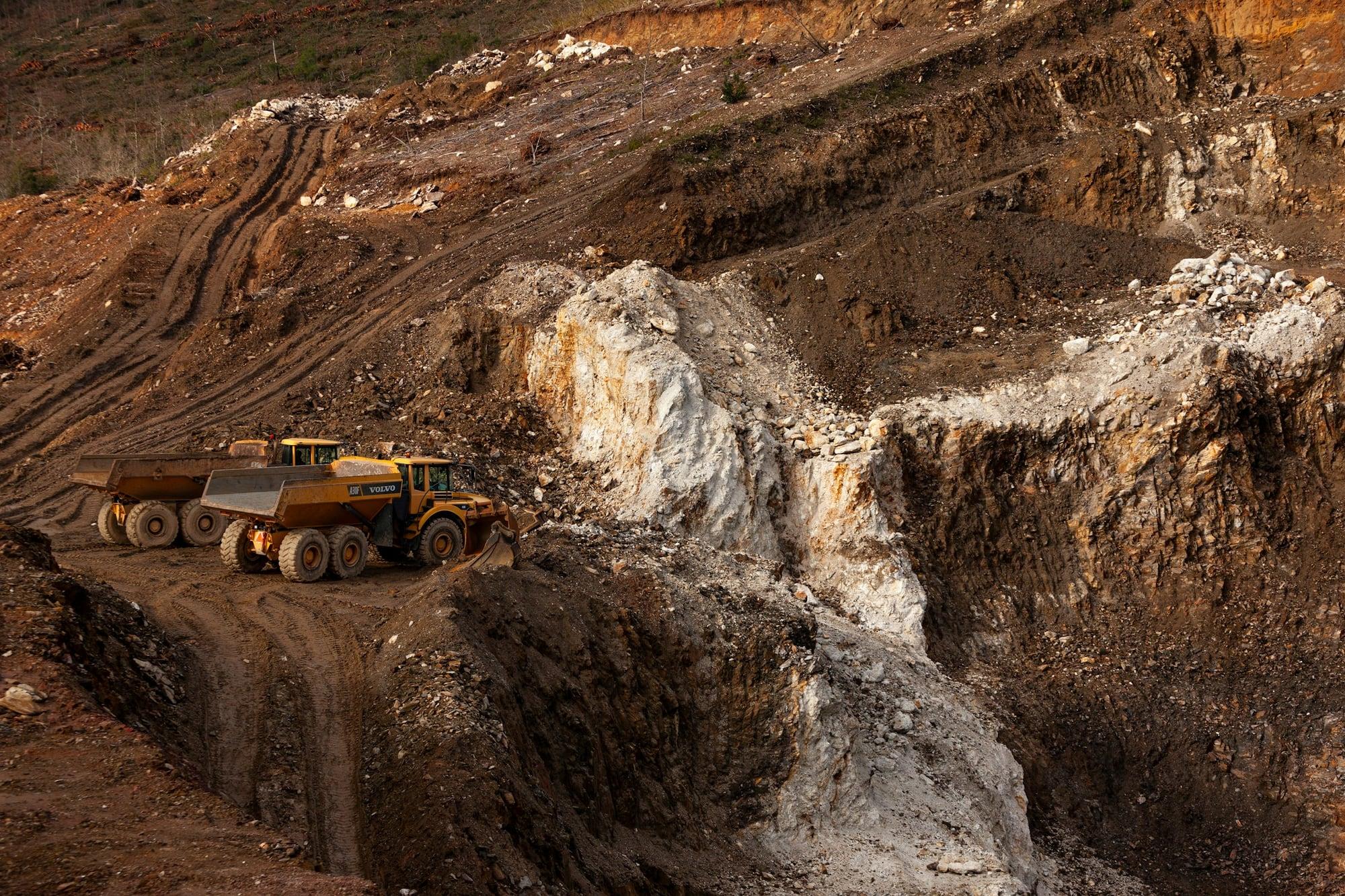 Open-pit mine terraces at sunset with haul trucks on the access roads